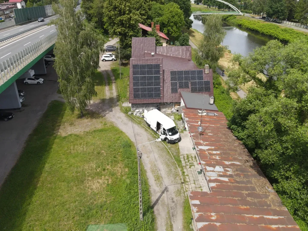 Szerokokątny widok na budynek z zamontowanymi panelami fotowoltaicznymi oraz otaczający teren.